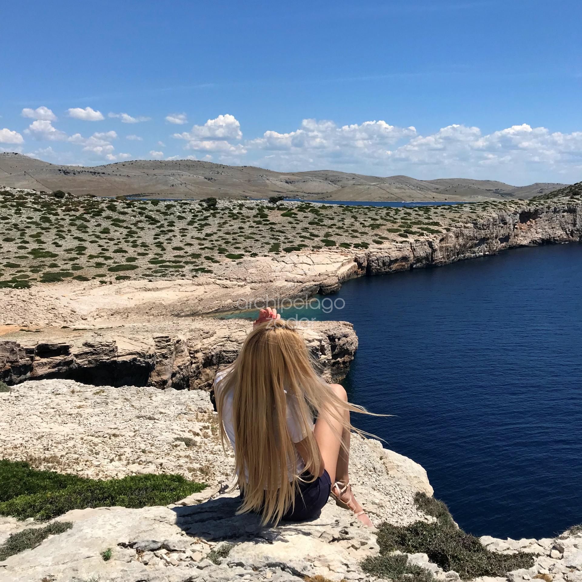 Girl sitting on a cliff in kornati islands long hair blonde